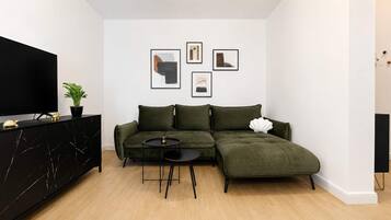 En moderne stue med en modulsofa, et fladskærms-tv, et lille rundt bord og billedkunst på væggen.