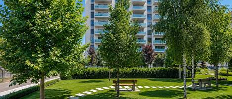 A park with benches, trees, and a modern apartment building in the background.