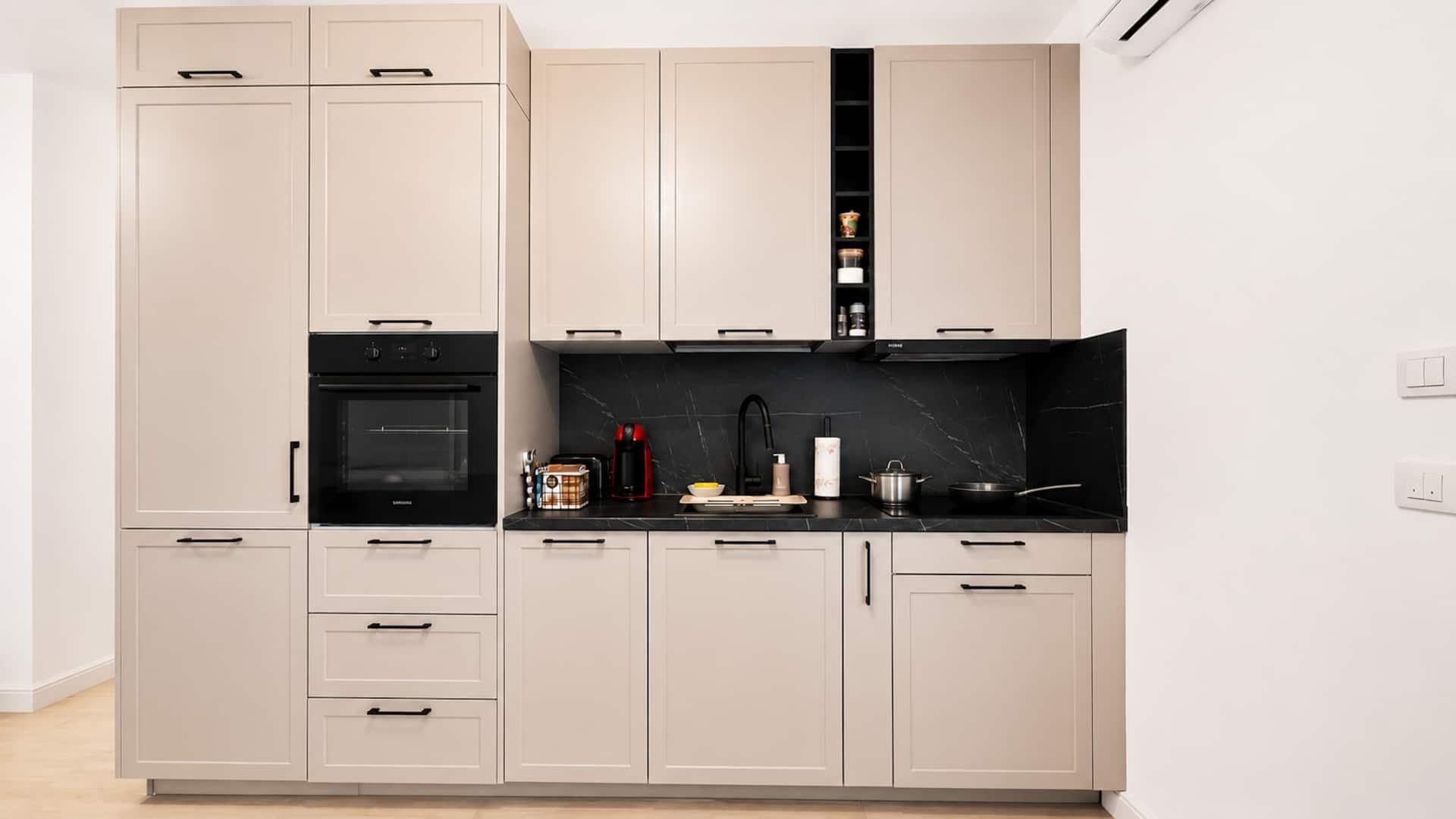 Eine moderne Küche mit hellen Schränken, einer schwarzen Arbeitsplatte und einem eingebauten Backofen.