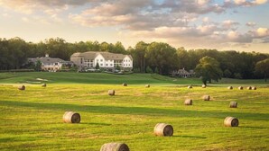A large field with multiple hay bales and a large building in the background. - Pursell Farms (Sylacauga)