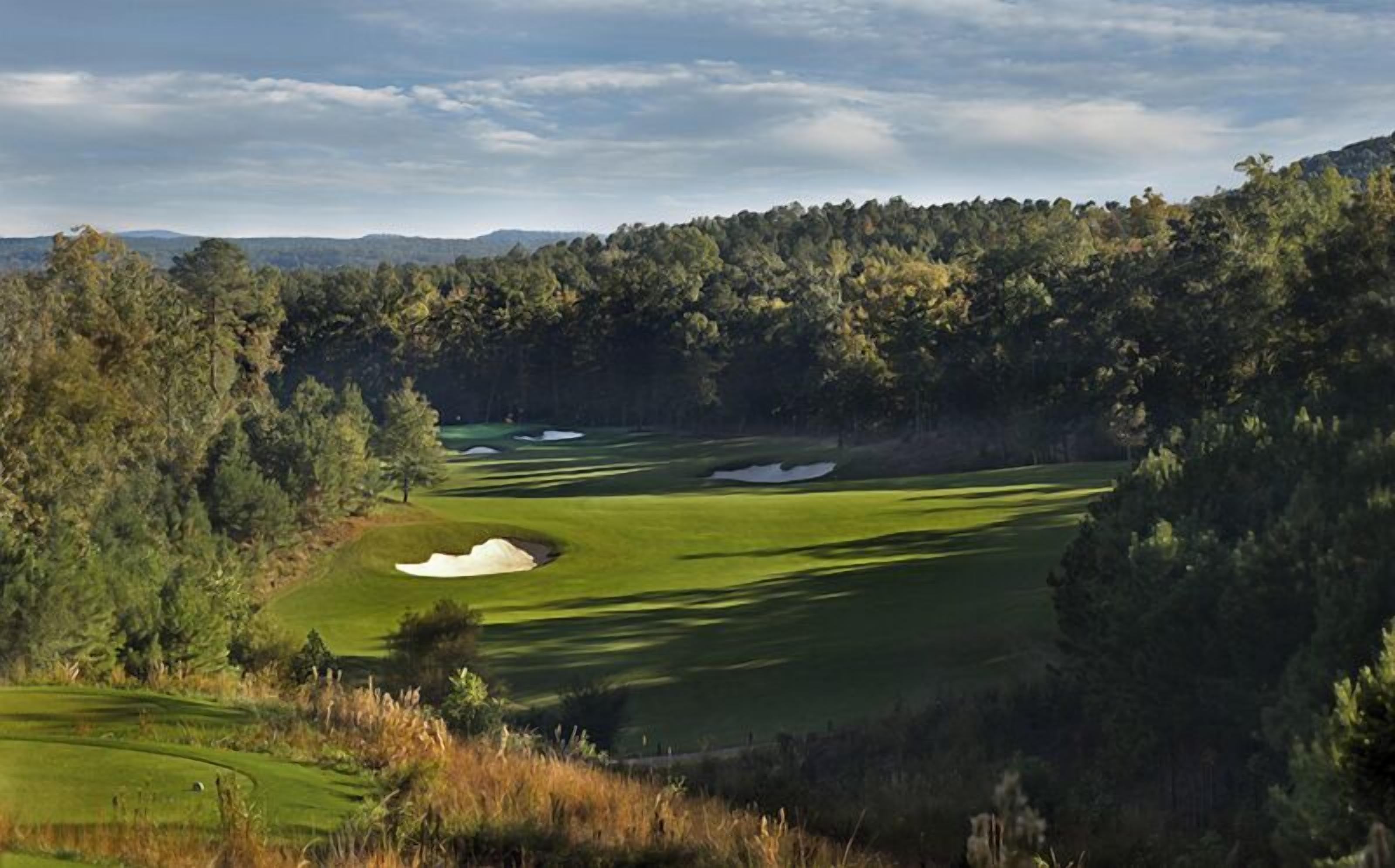 A golf course with sand bunkers and a forested backdrop.