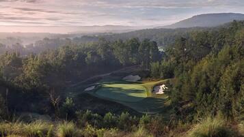 A golf course surrounded by dense forest and hills.
