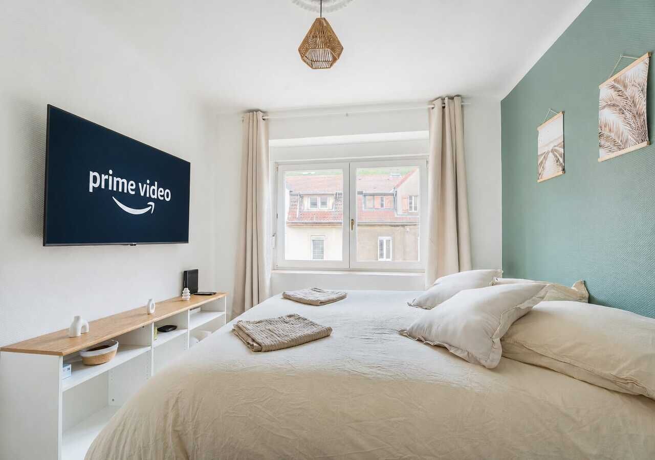 Ett hotellrum med en säng, en tv som är monterad på väggen, ett fönster med gardiner och konstverk på väggen.