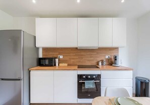 Eine kompakte Küche mit weißen Schränken, einem Edelstahl-Kühlschrank, einem Einbauofen und einer Kaffeemaschine auf der Arbeitsfläche.