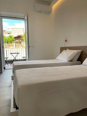 Habitación de hotel con dos camas, un balcón y aire acondicionado.