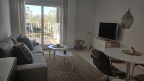 A modern living room with a sofa, coffee table, TV, and a balcony with outdoor furniture. - Exclusive Silent & Sunny Top Floor Apartement, 2 Pools & Golfview (Roldan)