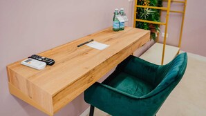 Un escritorio de madera con un control remoto, un bolígrafo y botellas de agua. Una silla verde está colocada frente al escritorio.