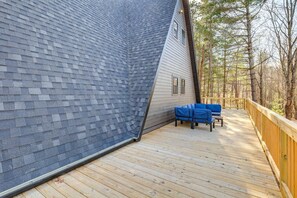 Eine Holzterrasse mit einem blauen Sofa, einem Holengeländer und einem Haus mit geneigtem Dach.