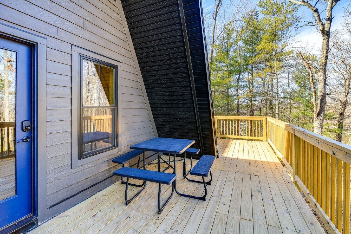 A deck with a table and benches, a blue door, and a view of trees.