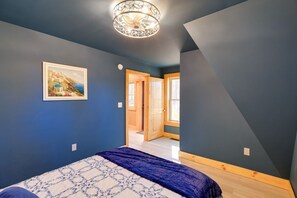 A bedroom with a bed, a painting, a ceiling light fixture, and a door leading to another room. - Chimney Rock Chalet w Mountain Views Near Main St (Wytheville)
