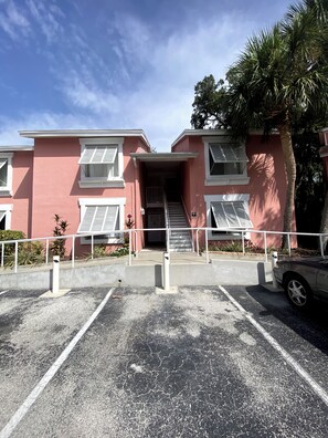 A building with a pink facade, white windows, and a staircase leading to an entrance. - Waterfront 1 BR Condo Private Beach, Pool & Sunset Views 30 DAY MIN (St. Petersburg)