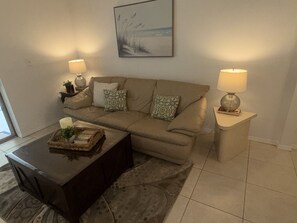 A living room with a sofa, two side tables with lamps, a coffee table, and a framed picture on the wall. - Waterfront 1 BR Condo Private Beach, Pool & Sunset Views 30 DAY MIN (St. Petersburg)