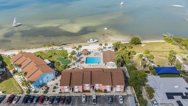 Vista aérea de uma propriedade costeira com piscina, acesso à praia e carros estacionados.