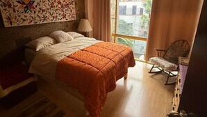 A bedroom with a bed, a chair, a window, and a wall with a colorful painting. - Beautiful Condesa Private Apartment (Ciudad de México)
