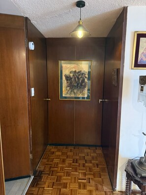 A wooden door with a framed artwork above it, a patterned wooden floor, and a hanging light fixture. - Beautiful Condesa Private Apartment (Ciudad de México)