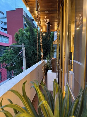 A balcony with hanging decorations, a potted plant, and a view of buildings in the background. - Beautiful Condesa Private Apartment (Ciudad de México)