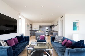A modern living room with a sofa set, a coffee table, and a kitchen in the background.