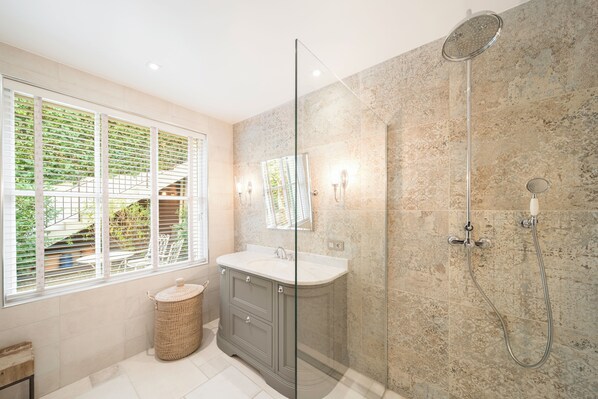 A modern bathroom with a glass shower enclosure, a vanity with a mirror, and a window with blinds.