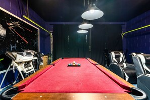 A pool table with a red felt surface, surrounded by black and white cushioned chairs, and overhead lighting fixtures. - 5BR Pool Home-Spa-Epic Game Room Near Disney (Davenport)