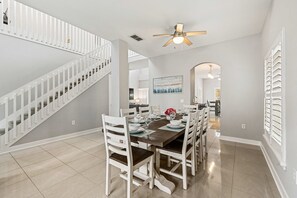 A dining area with a wooden table, white chairs, and a staircase with white railings. - 5BR Pool Home-Spa-Epic Game Room Near Disney (Davenport)