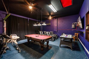 Ein Billardtisch in einem Raum mit violetten Wänden und Deckenventilatoren.