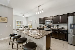 A modern kitchen with dark wood cabinets, stainless steel appliances, a granite countertop, and a central island with bar stools. - 5BR Pool Home-Spa-Epic Game Room Near Disney (Davenport)