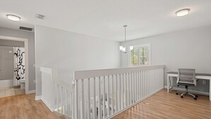 Ein geräumiger Raum mit Holzboden, weißer Geländer, einem Schreibtisch mit Stuhl und einem Fenster mit Jalousien.