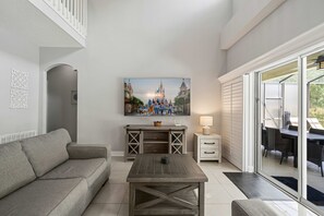 A living room with a sofa, a coffee table, a TV, and a dining area with chairs and a table. - 5BR Pool Home-Spa-Epic Game Room Near Disney (Davenport)