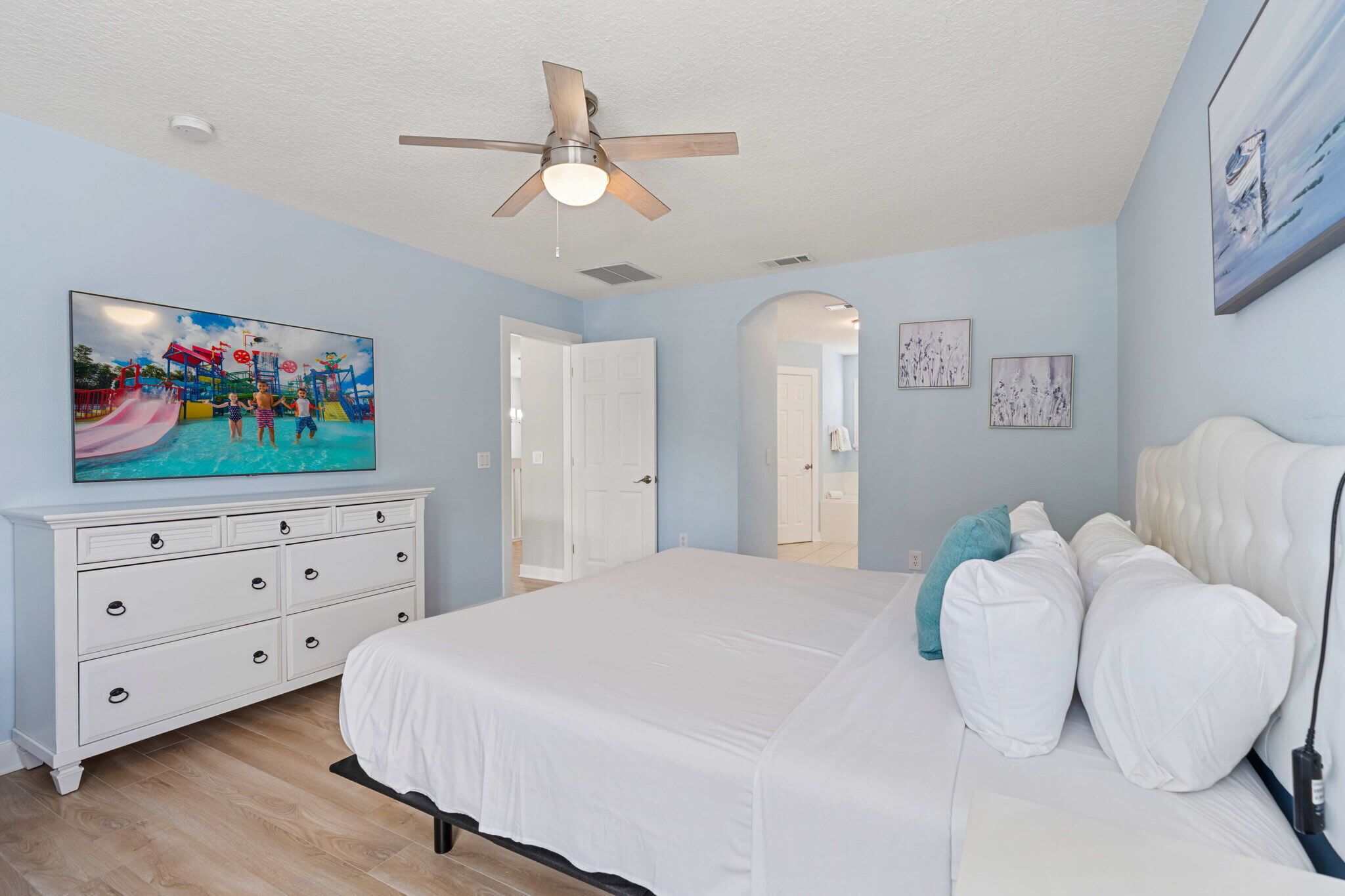 Een slaapkamer met een bed, een witte dressoir, een plafondventilator en een schilderij van een waterpark.
