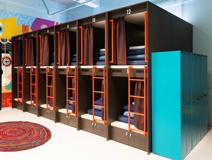A row of bunk beds with numbers, a colorful wall mural, and a teal-colored wardrobe.