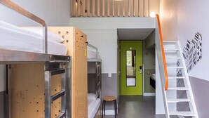 Una camera del dormitorio con letti a castello, uno sgabello, una porta verde e una scala bianca.