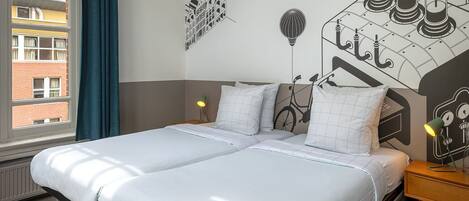A double bed with white bedding, a nightstand with a lamp, and a wall mural with bicycles and hot air balloons.
