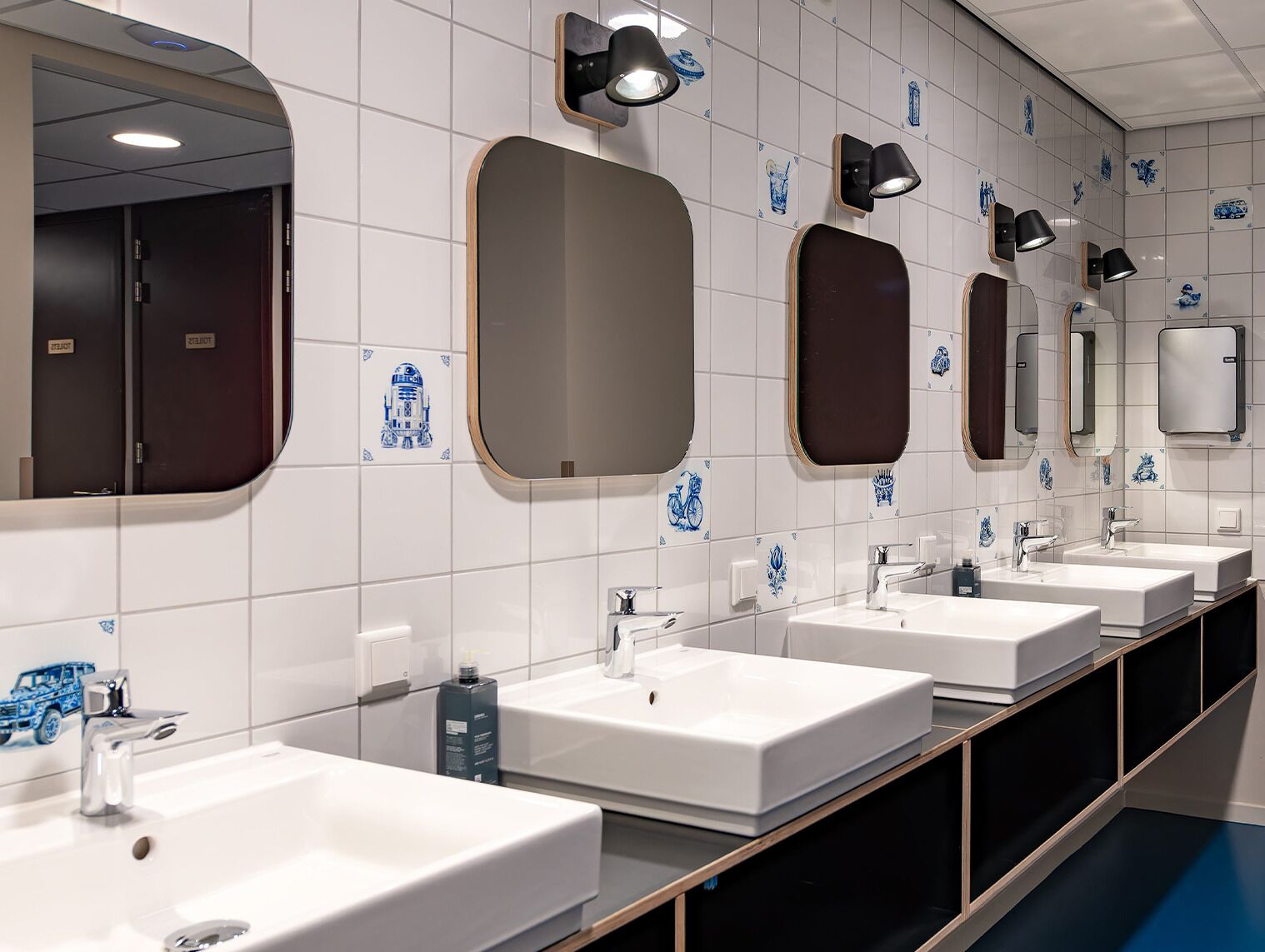 A row of sinks with mirrors and wall-mounted lights in a public restroom.