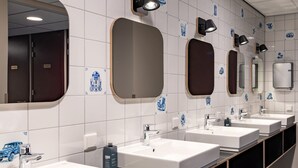 File di lavandini con specchi e luci a parete in un bagno pubblico.