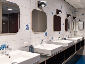 A row of sinks with mirrors and wall-mounted lights in a public restroom. - Stayokay Hostel Groningen (Groningen)