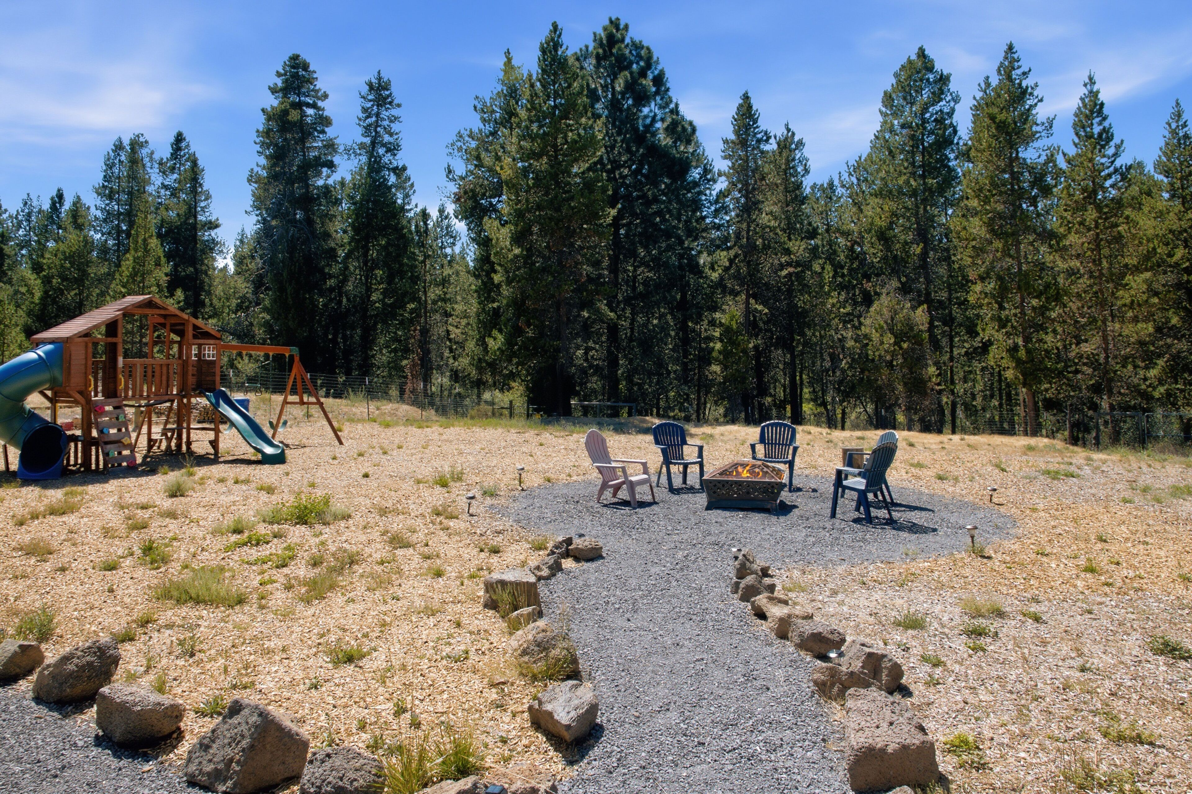 A playground with a slide and swings, surrounded by a forest.
