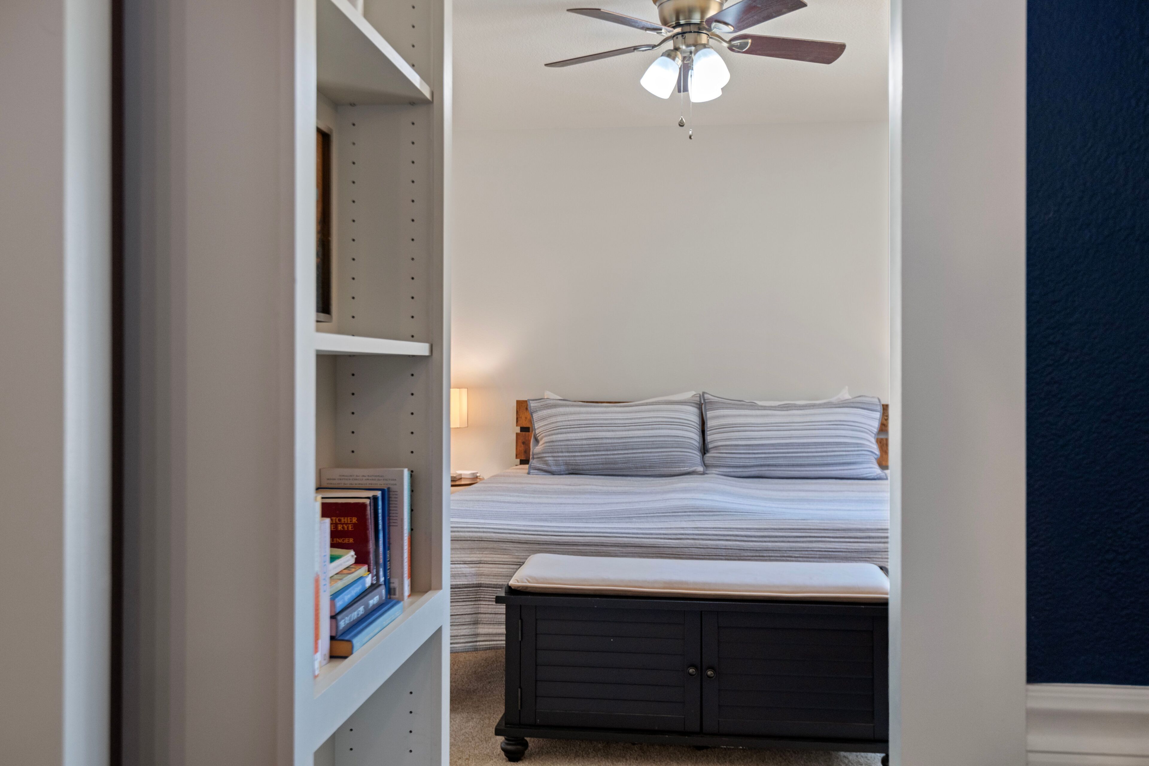 Una camera da letto con un letto, un comodino, una libreria e una ventola a soffitto.