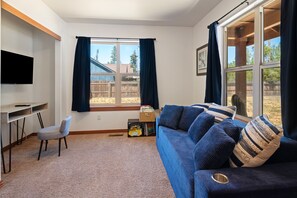 A modern living room with a blue sofa, a TV mounted on the wall, and a window with curtains. - South of Sunriver - Near Mt Bachelor - Hot Tub (Bend)