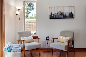 Une pièce comprenant deux fauteuils, une petite table, une lampe et un tableau représentant un paysage de montagne.