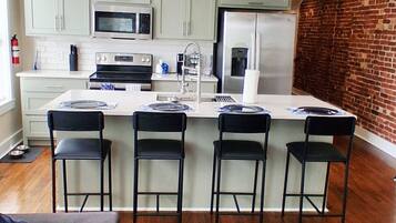 A modern kitchen with a central island, bar stools, and a ceiling fan.