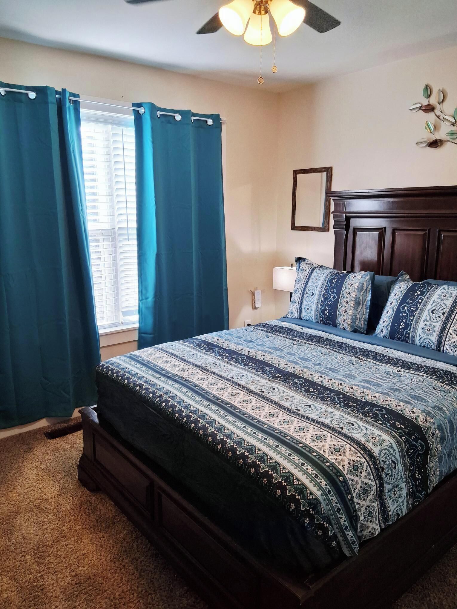 A bedroom with a bed, a ceiling fan, a window with curtains, and a wall-mounted light.