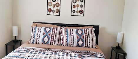 Un dormitorio con cama, dos adornos en la pared, ventilador de techo y lámparas de noche.