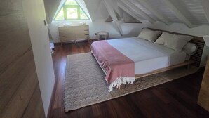 Et soveværelse med seng, kommode, vindue og skråt loft.