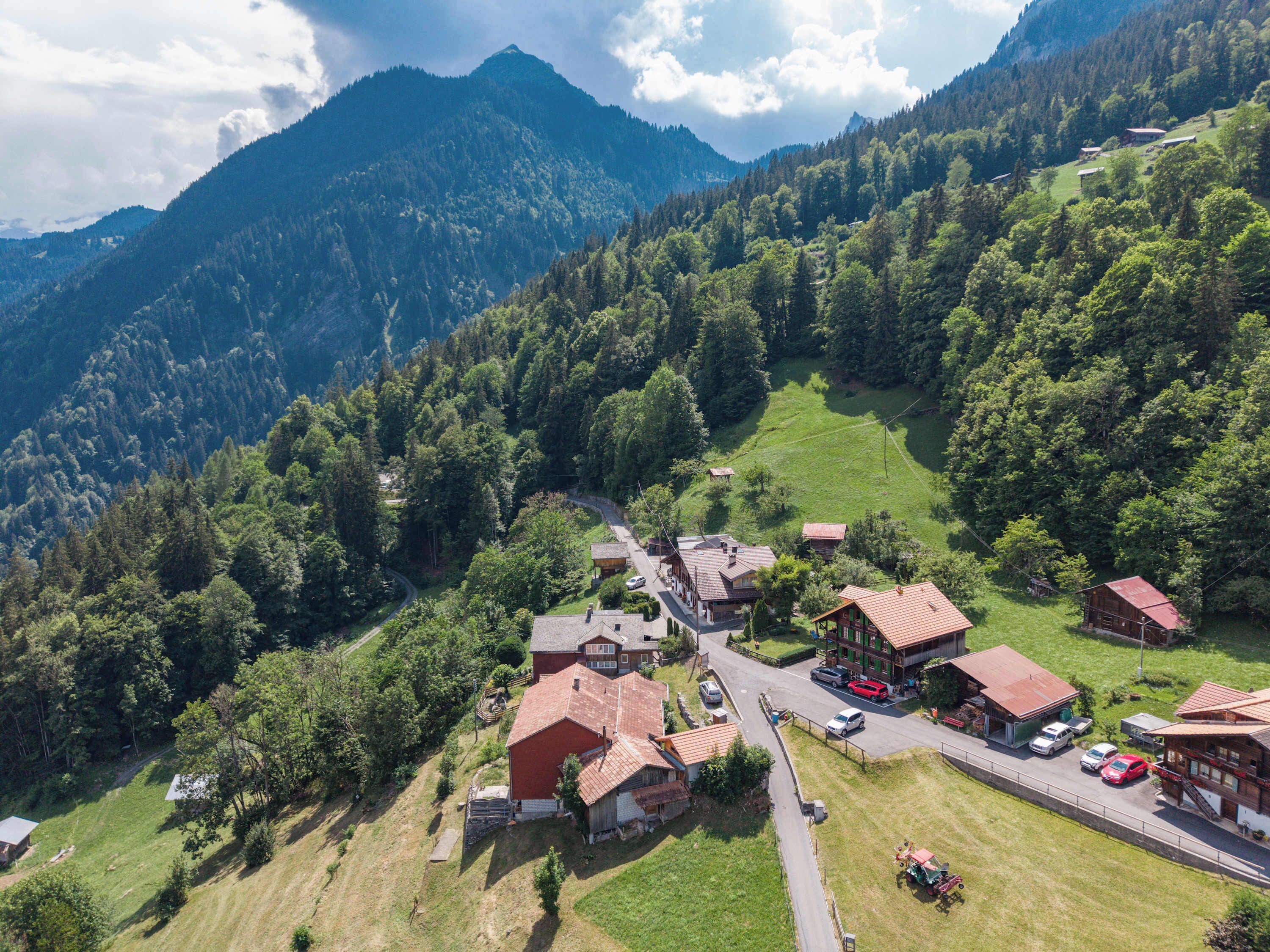 A rural mountain village with traditional wooden houses, a main road, and a mountain backdrop.