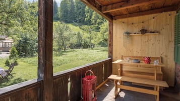 Une terrasse en bois avec un banc et une table, donnant sur un paysage verdoyant avec des arbres et une maison.