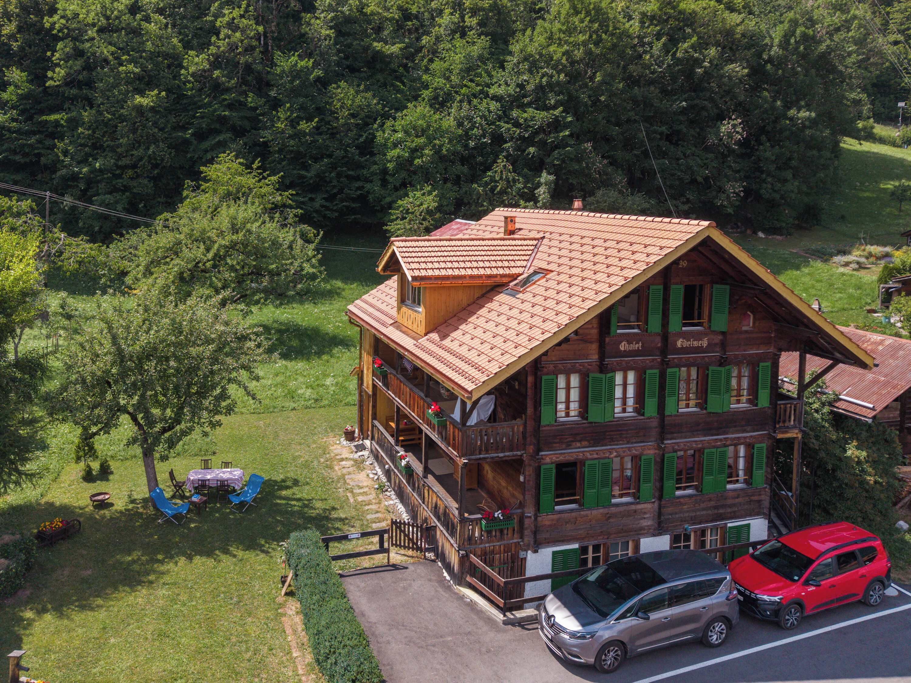 Un chalet en bois doté d’un balcon, une voiture garée devant, et un paysage verdoyant luxuriant.