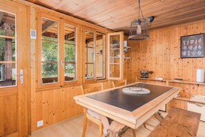 A wooden interior with a dining table, chairs, a hanging light fixture, and wooden walls.