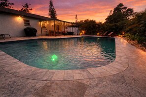 A swimming pool with a curved edge, surrounded by a patio area with a covered seating area and a building in the background. - Guest Favorite! Tropical Oasis / Luxury Pool (Largo)