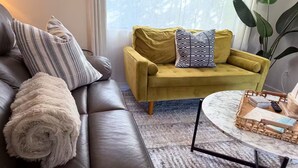 Ein Wohnzimmer mit einem dunkelbraunen Ledersofa, einem gelben Sessel und einem runden Couchtisch mit einem gewebten Tablett.