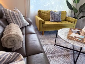 A living room with a dark leather sofa, a yellow armchair, and a round coffee table with a woven tray. - Guest Favorite! Tropical Oasis / Luxury Pool (Largo)